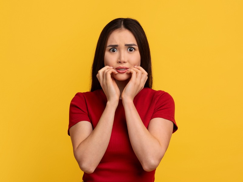 Jeune femme asiatique effrayée touchant son visage, fond de mur jaune.