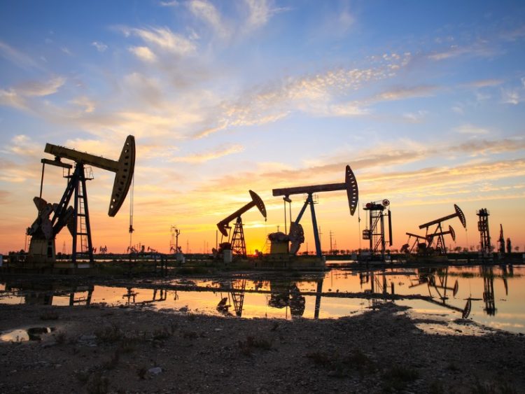Site du champ pétrolifère, le soir, les pompes à huile fonctionnent, La pompe à huile et le magnifique coucher de soleil se reflètent dans l’eau.