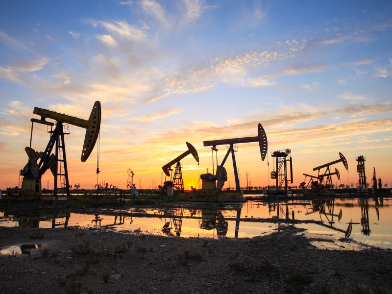 Site du champ pétrolifère, le soir, les pompes à huile fonctionnent, La pompe à huile et le magnifique coucher de soleil se reflètent dans l’eau.