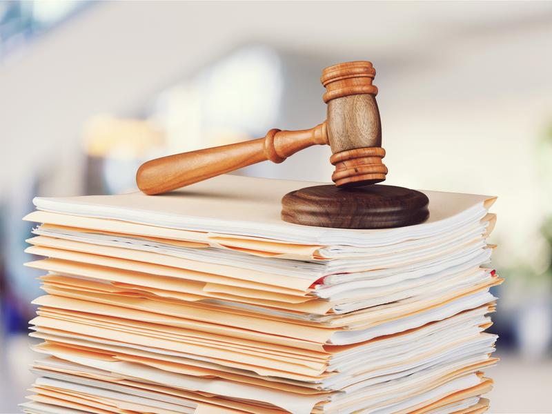 Gros maillet de juge posé sur une pile de dossiers et de documents jaunâtres. Image à connotation juridique.