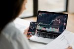 Femme analysant des graphiques boursiers sur un ordinateur portable et un smartphone. Concept d’investissement en ligne et de suivi des marchés financiers en temps réel.