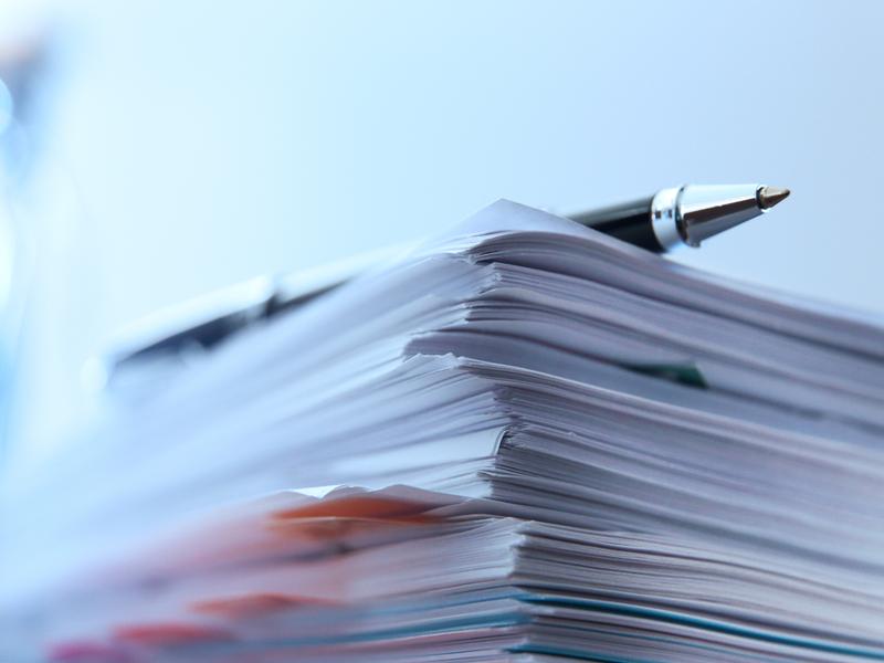 Pile de documents avec un stylo à bille posé sur le dessus. Ambiance bleu clair, mise au point sur l’épaisseur des feuilles.
