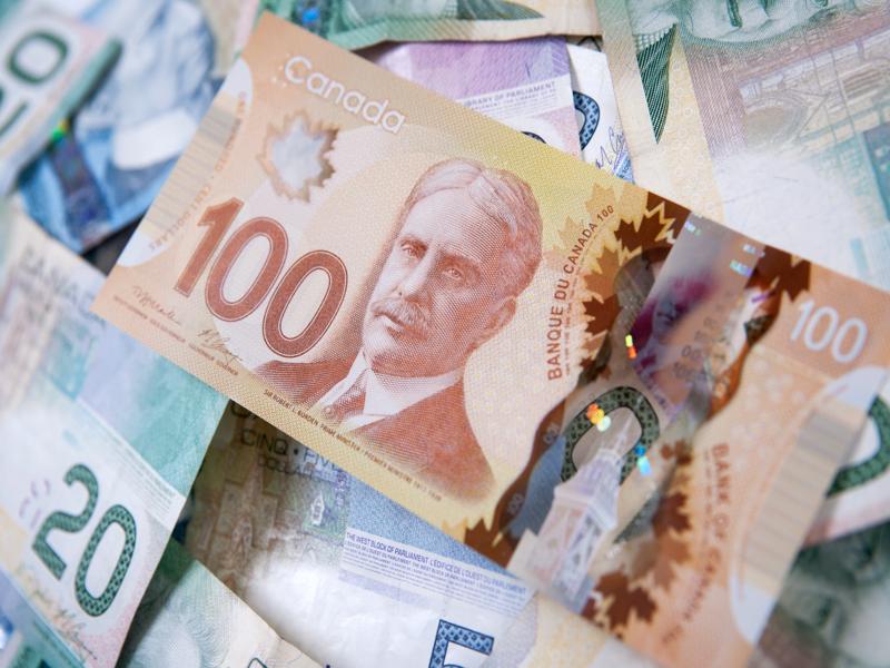 Billet canadien de 100 $ en gros plan, posé sur un amas de billets de différentes coupures.