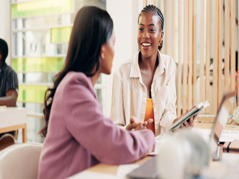 Deux femmes discutant dans un environnement de bureau lumineux et moderne.