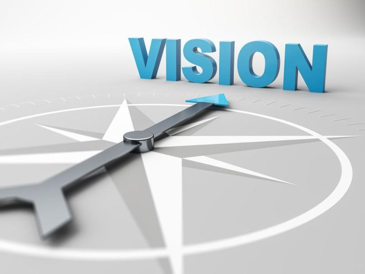 Une boussole grise avec une flèche bleue pointant vers le mot « VISION » en 3D. Illustration symbolique de l’orientation et de la vision d’avenir.