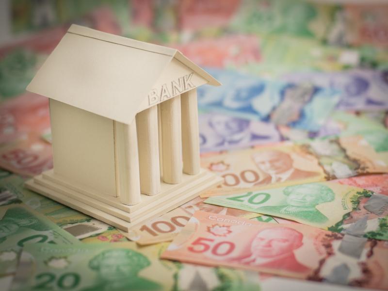 Maquette d’une banque en bois placée sur des billets canadiens multicolores.