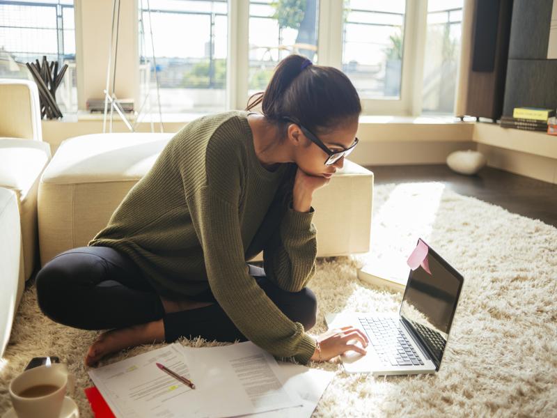 Jeune femme assise au sol, concentrée sur ses documents et son ordinateur.