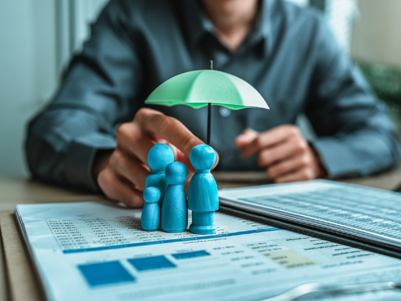 Une poupée en bois sous un parapluie tenue par l’agent représentent l’assurance. La famille, la protection, la vie.