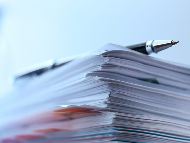 Une pile de documents administratifs illustre le traitement et la gestion de dossiers.
